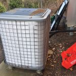 A metal air conditioner positioned outdoors beside a trash can, showcasing a typical urban environment.