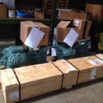Two large green air compressors positioned on pallets within a warehouse setting, showcasing industrial equipment storage.