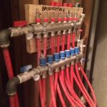 A wall-mounted water heater featuring red pipes and valves, showcasing its functional design and plumbing connections.