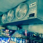 A wall featuring a ceiling fan above a collection of assorted cans arranged neatly below.